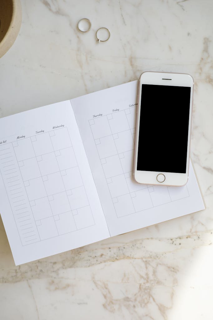 A smartphone and open planner on a marble table with rings, ideal for business and organization themes.
